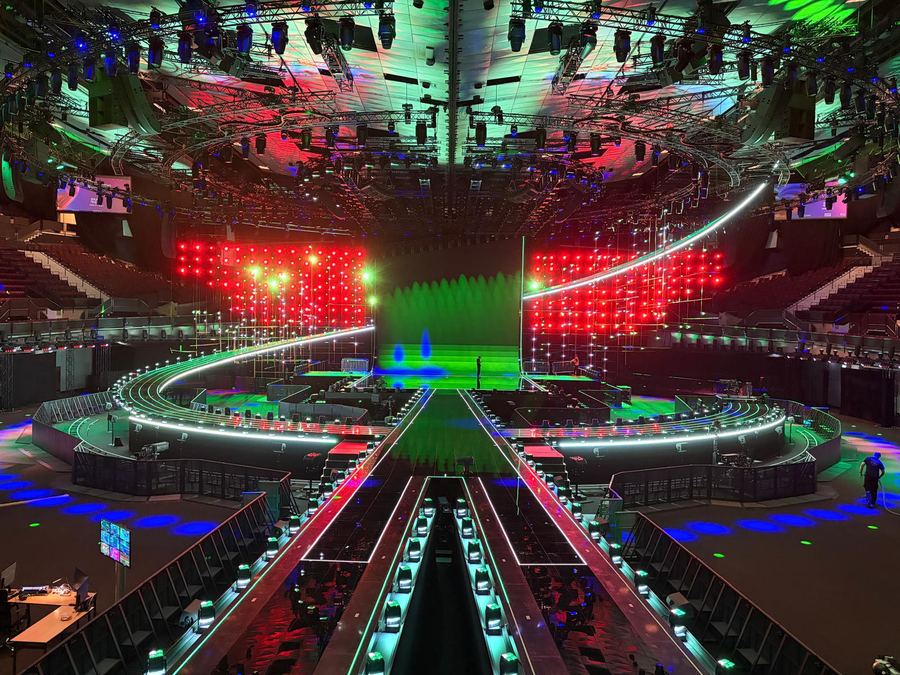 Arena stage under a curved roof with lighting truss and a rigger on a line