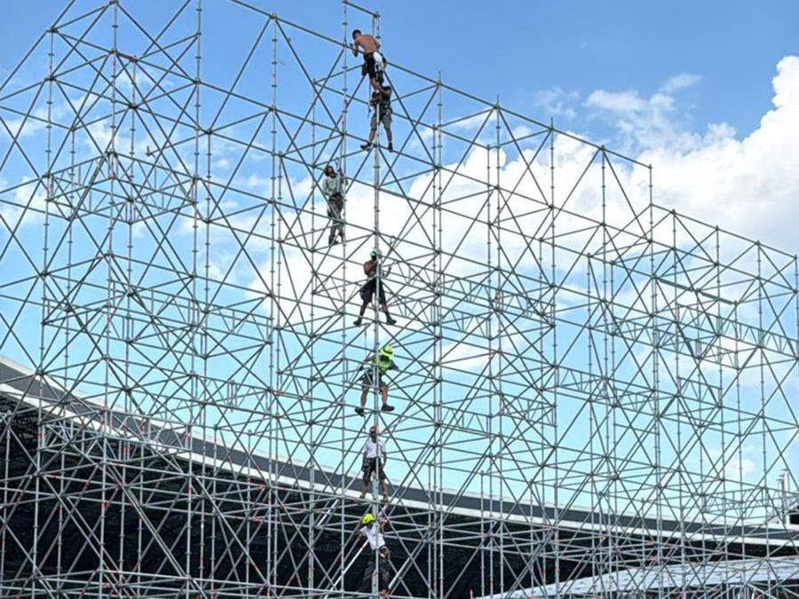 Rigger climbing a tall scaffold tower at a stadium