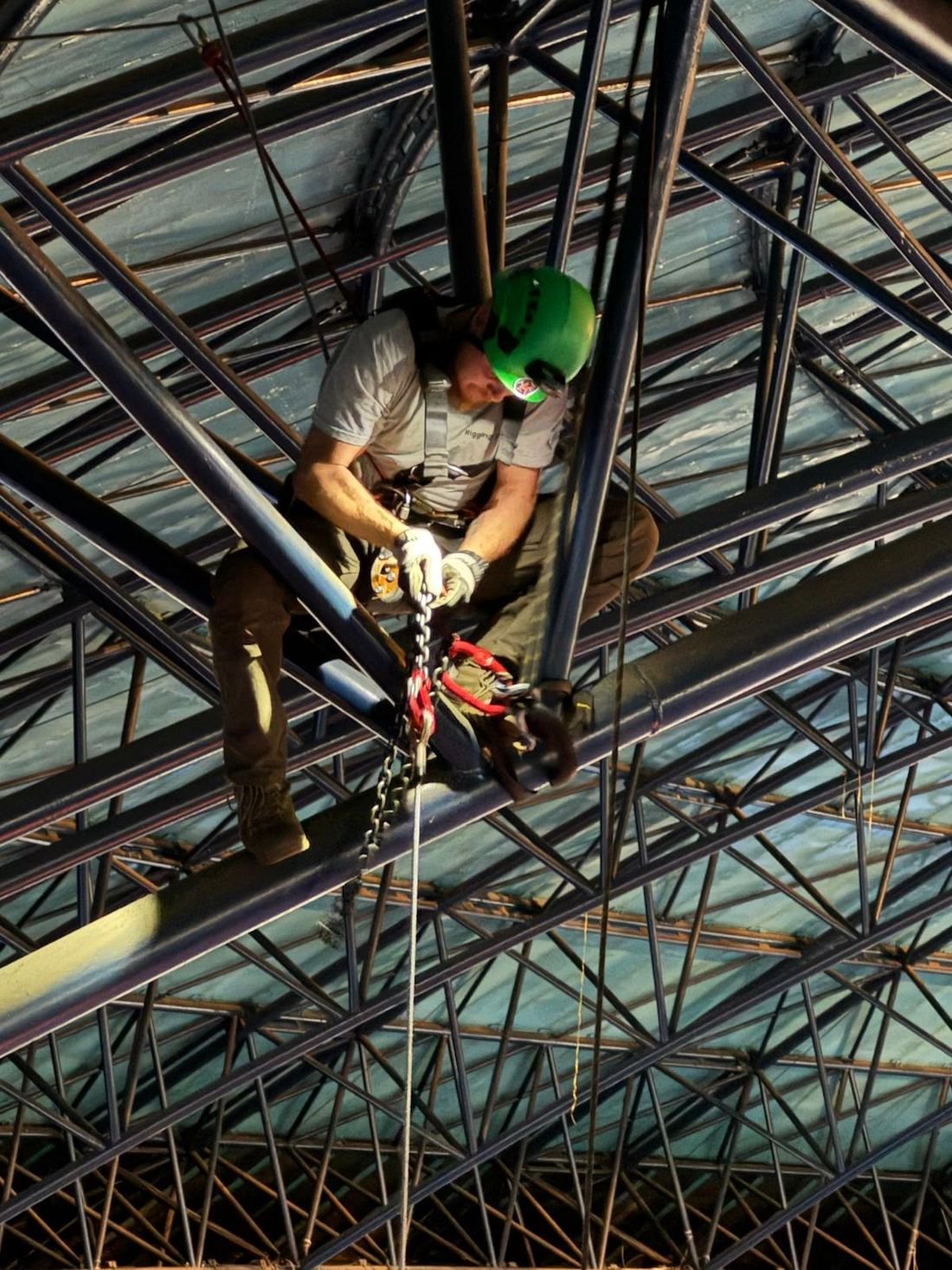 Rigger securing a chain hoist on a steel truss structure at height